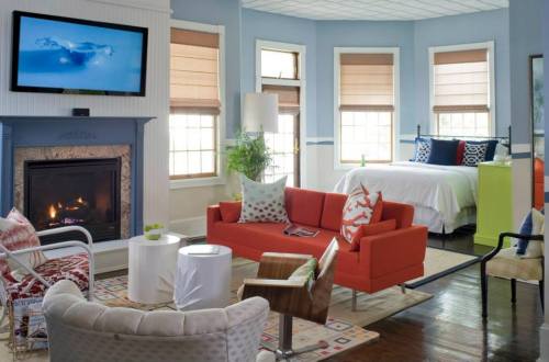 Cozy living space featuring a fireplace, orange sofa, and a bedroom area with a bed and colorful decor.