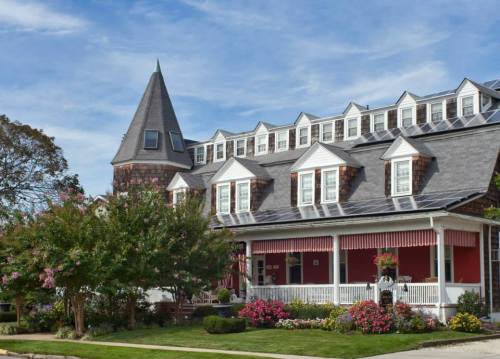 A charming multi-story building with a pointed roof, surrounded by colorful flowers and greenery under a blue sky.