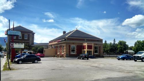 A historic building with a red and cream facade, surrounded by parked cars under a blue sky with scattered clouds.