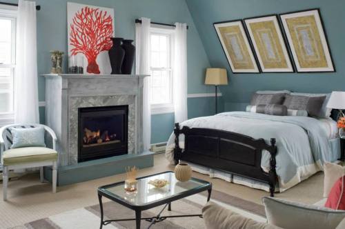 Cozy bedroom with a fireplace, blue walls, coral artwork, and modern decor, featuring a bed and seating area.