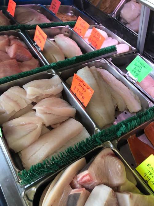 Display of various fresh fish fillets in trays, labeled with colorful price tags.