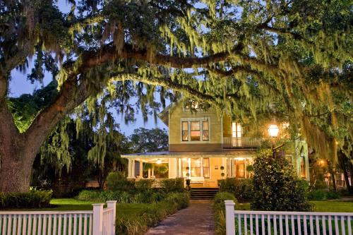 A charming house with a porch, surrounded by lush greenery and draped in Spanish moss under a twilight sky.