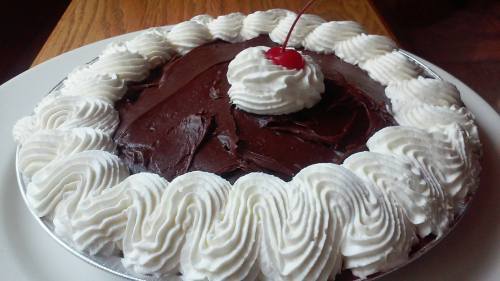 A chocolate pie topped with whipped cream and a cherry in the center, served on a white plate.