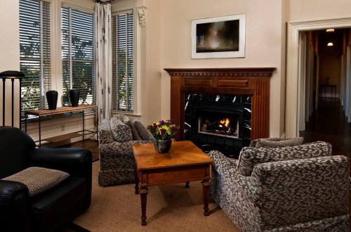 Cozy living room with two patterned armchairs, a wooden table, and a fireplace, surrounded by large windows.
