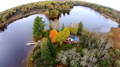 Aerial view of a serene lake surrounded by colorful autumn trees and a small cabin near a dock.