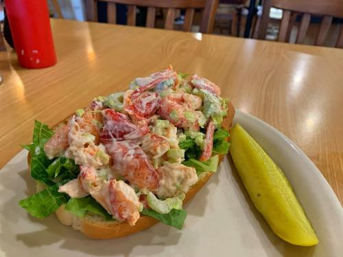 A lobster roll topped with lettuce and a creamy dressing, served with a pickle on the side.