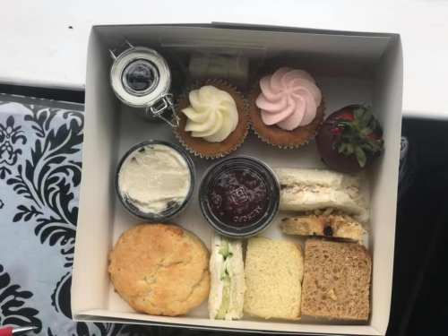 A box filled with assorted treats: cupcakes, cookies, sandwiches, and jars of jam and cream.