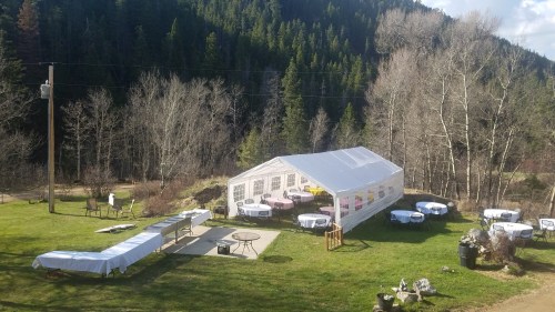 A large white tent set up on a grassy area, surrounded by trees, with tables and chairs arranged for an event.
