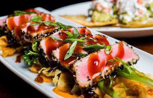 A plate of seared tuna slices on a bed of crispy chips, garnished with green onions and drizzled with sauce.