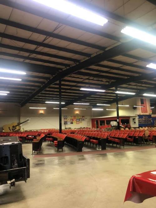 Empty indoor venue with rows of red chairs, high ceilings, and stage area, featuring a large guitar decoration.