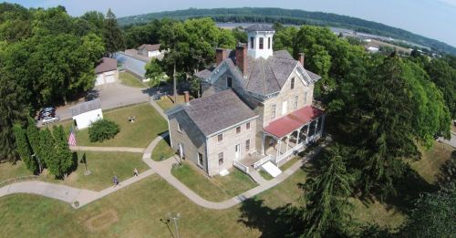 Aerial view of a historic stone house surrounded by trees and pathways, with a flagpole in the foreground.
