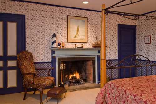 Cozy bedroom with a four-poster bed, armchair, and a fireplace, featuring floral wallpaper and nautical decor.