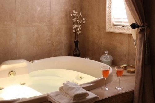 A luxurious bathroom with a jetted tub, two glasses of pink drink, and decorative elements in warm tones.