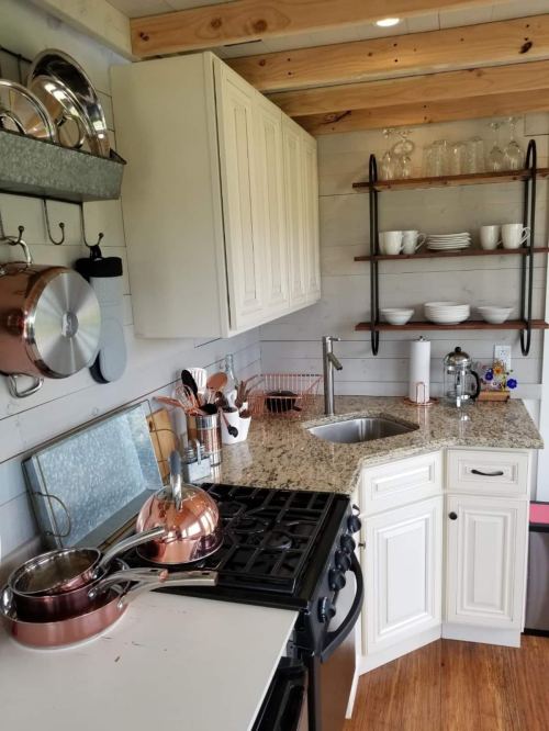 Cozy kitchen with white cabinets, granite countertops, and copper cookware, featuring open shelves and a modern sink.