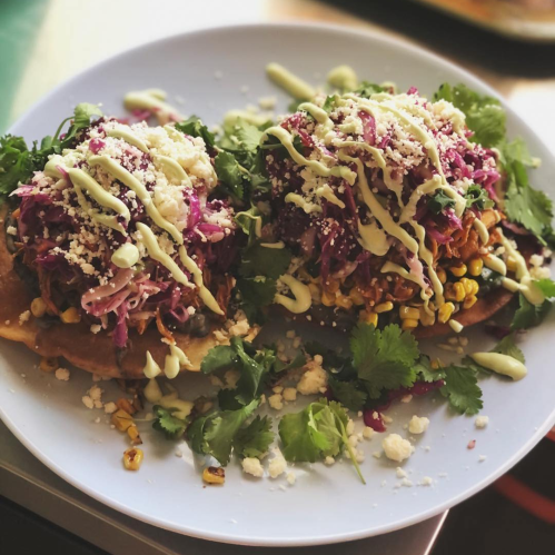 Two colorful tostadas topped with shredded cabbage, corn, cheese, and drizzled with green sauce, garnished with cilantro.