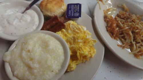 A plate of breakfast featuring scrambled eggs, grits, a biscuit, bacon, and hash browns.
