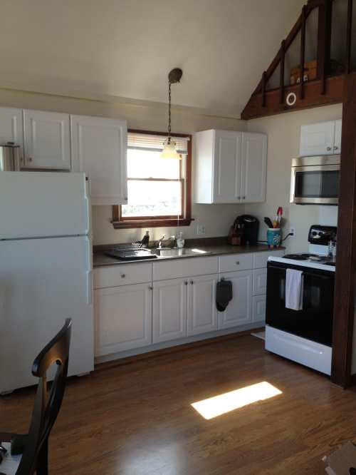 Bright kitchen with white cabinets, a black stove, and a refrigerator, featuring wooden floors and natural light.