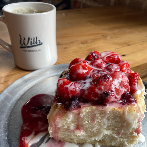 A plate with a dessert topped with strawberries and cream, next to a cup of coffee on a wooden table.