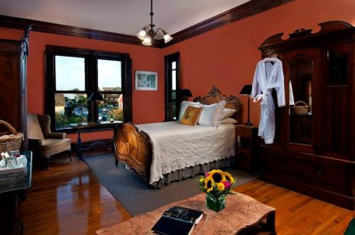 Cozy bedroom with a wooden bed, orange walls, a floral arrangement, and a robe hanging in a vintage-style setting.