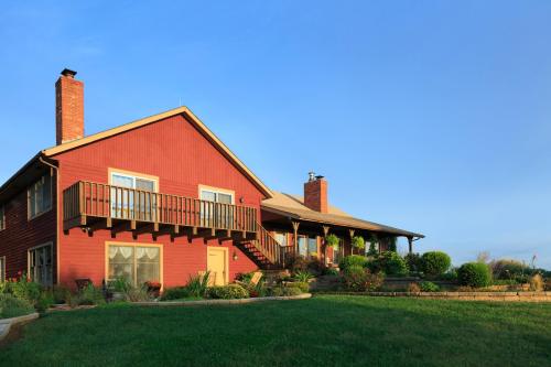 A red two-story house with a balcony, surrounded by greenery and a clear blue sky.
