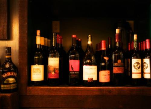 A wooden shelf displaying various bottles of wine and a bottle of Baileys on the left.