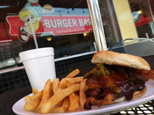 A burger with barbecue sauce and pickles, served with fries and a drink, in front of a Burger Bar sign.