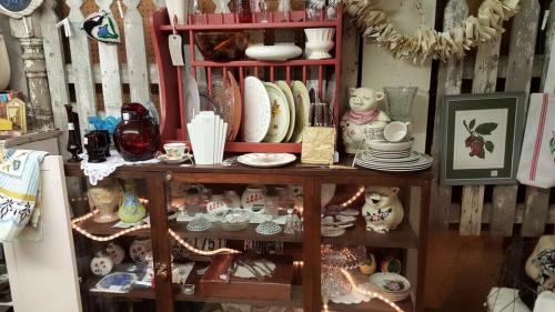 A vintage display featuring various dishes, glassware, and decorative items on a wooden shelf and cabinet.