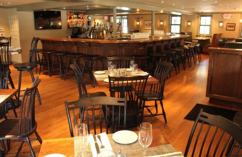 A cozy restaurant interior featuring wooden tables, chairs, and a bar area with a warm ambiance.