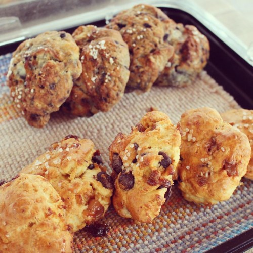 A tray of freshly baked scones with chocolate chips and a sprinkle of coarse salt, arranged on a woven mat.
