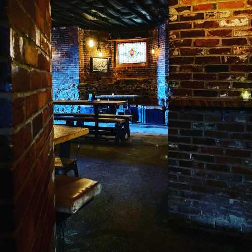 Cozy interior of a brick-walled room with wooden tables, dim lighting, and a stained glass window.