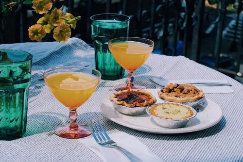 Two cocktails and a plate of desserts on a table, surrounded by green glasses and a striped tablecloth.