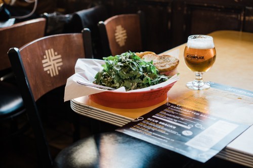 A bowl of fresh salad sits on a table next to a glass of beer and a menu in a cozy restaurant setting.