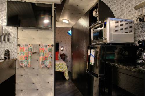 A compact kitchen area with a TV, microwave, and refrigerator, leading to a bedroom with patterned decor.