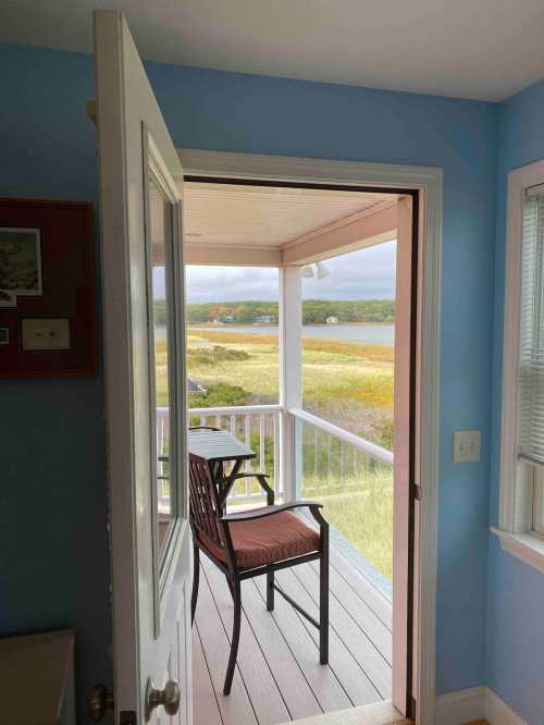 A view from an open door showing a porch with a chair overlooking a scenic landscape.