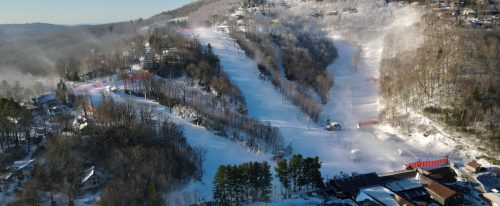 Aerial view of a snowy ski resort with slopes, trees, and misty mountains in the background.