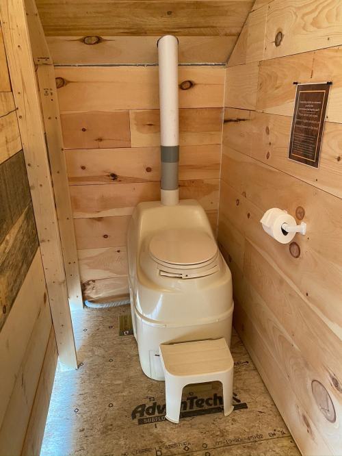 A compact, eco-friendly toilet in a wooden cabin, featuring a footstep stool and a roll of toilet paper nearby.