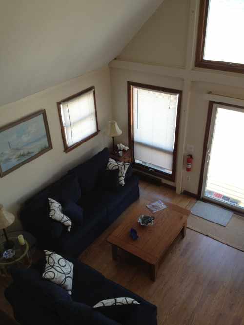 A cozy living room with two dark sofas, a wooden coffee table, and large windows letting in natural light.