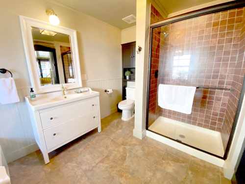 Bright bathroom featuring a white vanity, toilet, and a glass shower with pink tile accents.