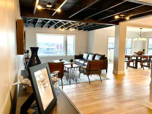 Modern living space with a leather sofa, wooden dining table, and large windows showcasing a city view.