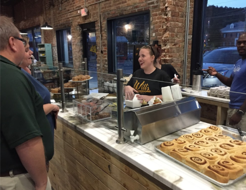 A smiling employee serves customers at a bakery with a rustic brick interior and a display of pastries.