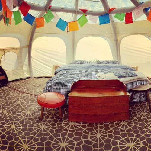 Cozy tent interior with a bed, wooden chest, and colorful prayer flags hanging from the ceiling.