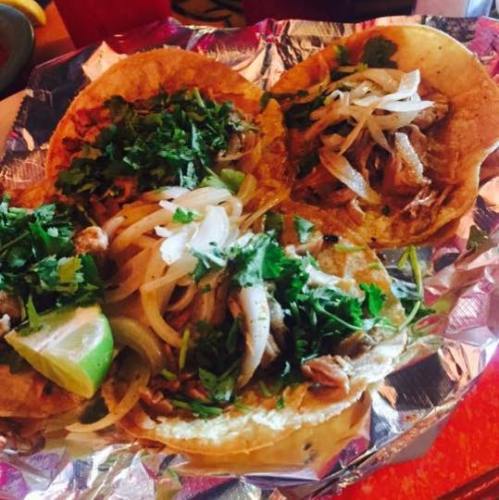 Three tacos filled with shredded meat, topped with onions, cilantro, and a lime wedge, served on foil.