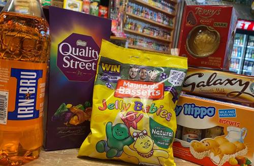 A variety of snacks and drinks, including Irn-Bru, Quality Street, Jelly Babies, and Galaxy chocolate, on a store shelf.