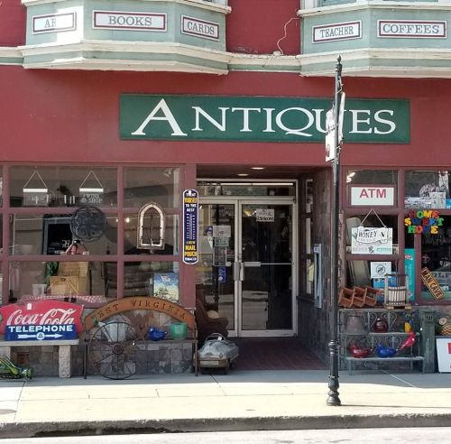 A storefront labeled "Antiques" with books, cards, and coffee signs, featuring an ATM and various decorative items outside.
