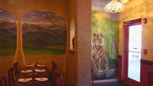Interior of a restaurant featuring mountain murals and a tiger painting, with tables set for dining.