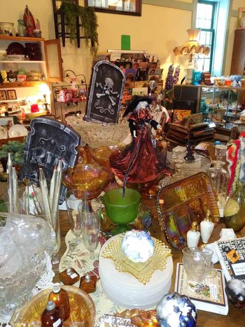 A cluttered display of various decorative items, including glassware, figurines, and Halloween-themed decorations.