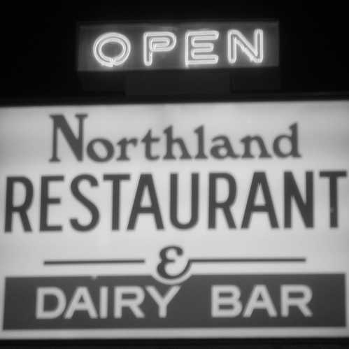 A black and white sign for Northland Restaurant & Dairy Bar, with an illuminated "OPEN" sign above it.