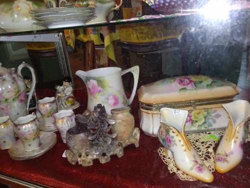 A display of vintage porcelain items, including a pitcher, decorative shoes, and various small figurines.