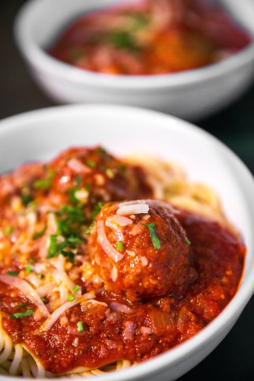 A close-up of spaghetti topped with meatballs and marinara sauce, garnished with herbs in a white bowl.