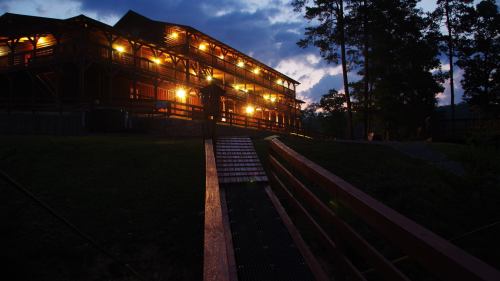 A wooden building illuminated at dusk, surrounded by trees and a pathway leading up to it.